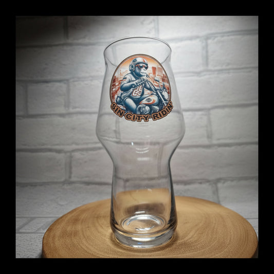 Glass of beer with a 'Sin City Kombucha' label on a wooden surface and white brick wall background