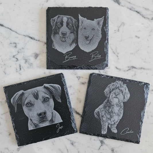 Set of custom slate coasters with engraved dog portraits on a marble surface. Staffy, Labrador, Beagle, Terrier, Collie, Bischon