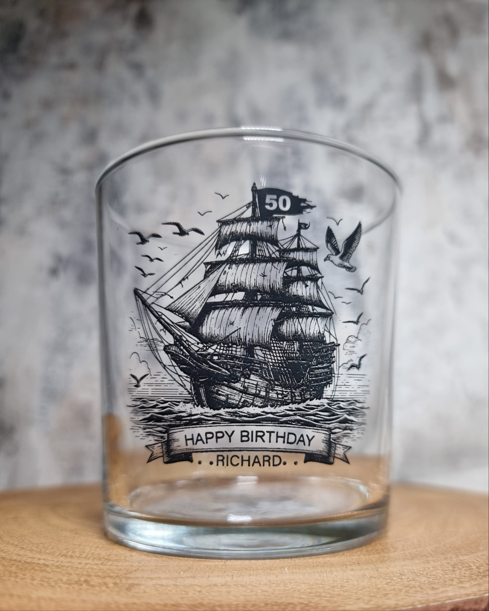 Personalised rum glass with ship design, custom name and age, shown with optional bamboo coaster and varnished wooden gift box – nautical themed gift for him