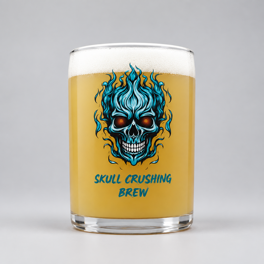 A clear glass pint mug filled with golden beer and topped with white foam, featuring a blue and black skull graphic with flames and the text 'SKULL CRUSHING BREW' on the front, photographed on a light gray background.