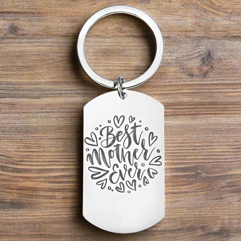 A stainless steel keyring with 'Best Mother Ever' engraved on it, displayed against a wooden background.