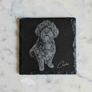 Close-up of laser engraved pet coaster showing detailed sketch-style dog portrait on dark slate