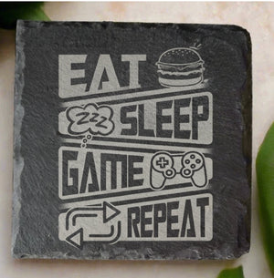 Eat Sleep Game Repeat laser engraved natural slate coaster 10cm x 10cm with gaming controller burger and sleep icons on light stone surface