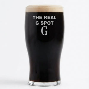A pint glass filled with black stout beer, featuring the white printed text 'THE REAL G SPOT' and a large letter 'G' on the front, topped with a thick head of foam, set against a plain white background.