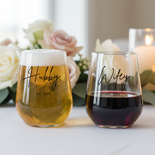Personalised 'Hubby & Wifey' stemless wine glass set with EST. 2026 engraving, filled with champagne and red wine, displayed with fresh flowers and candles in elegant setting