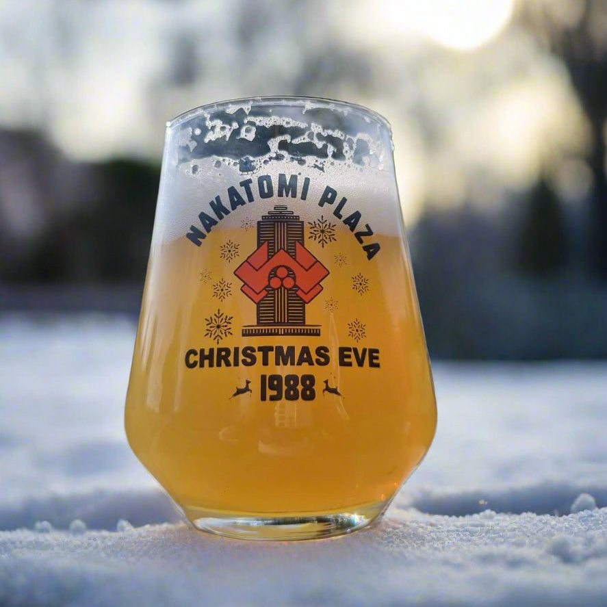 Nakatomi Plaza Christmas Eve 1988 stemless beer glass with vintage action movie graphic, filled with golden beer, placed in snow
