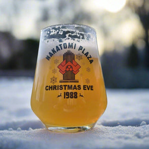 Nakatomi Plaza Christmas Eve 1988 stemless beer glass with vintage action movie graphic, filled with golden beer, placed in snow