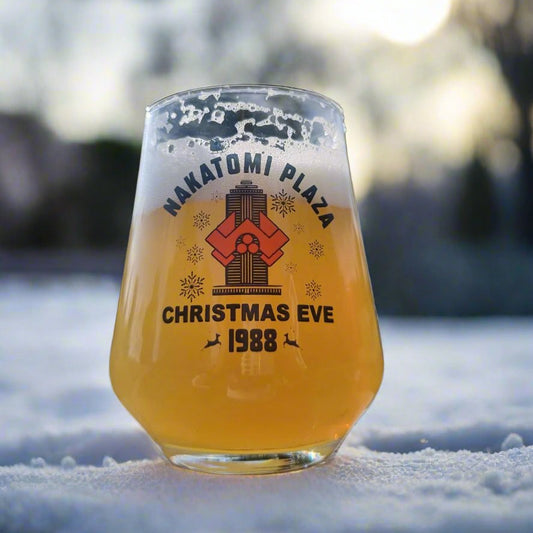 Nakatomi Plaza Christmas Eve 1988 stemless beer glass with vintage action movie graphic, filled with golden beer, placed in snow