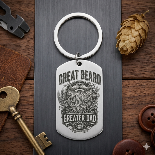 Keychain with 'Great Beard, Greater Dad' design on a wooden surface with tools and a pine cone.
