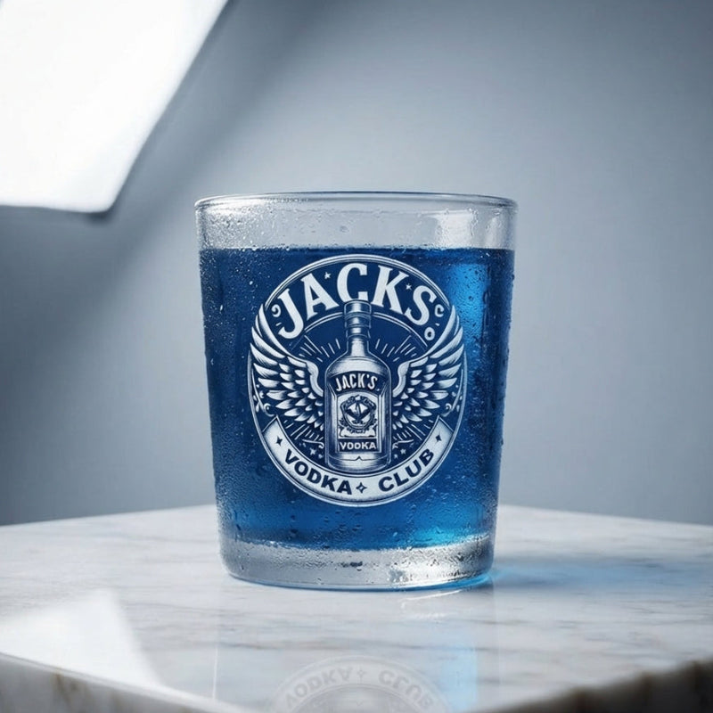 Personalised vodka club glass custom printed with bold winged badge crest design and personalised name displayed in a bar setting with spirit bottles in the backgroundDesigns