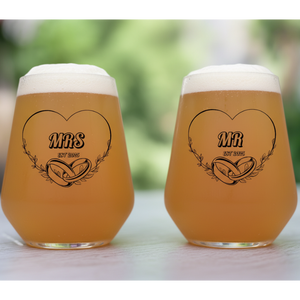 A personalized glass tumbler with 'Mr & Mrs' text and a heart design, filled with a beverage, displayed outdoors.