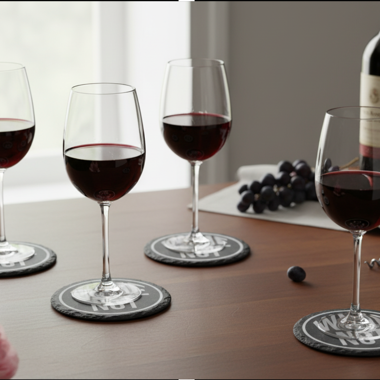 Wine glasses with red wine on a wooden table with grapes and a bottle.
