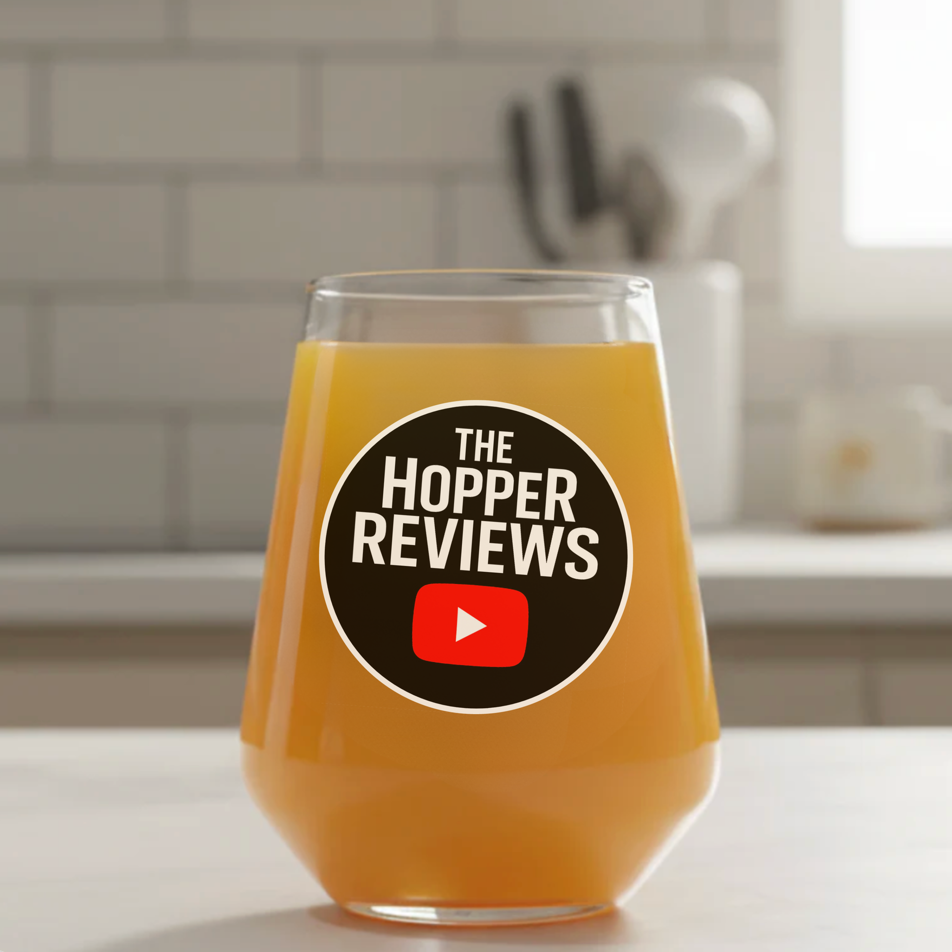 Official The Hopper Reviews collaboration beer glass with branded logo, filled with golden craft beer, kitchen setting
