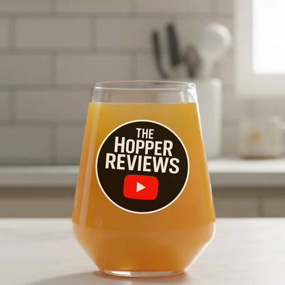 Official The Hopper Reviews collaboration beer glass with branded logo, filled with golden craft beer, kitchen setting