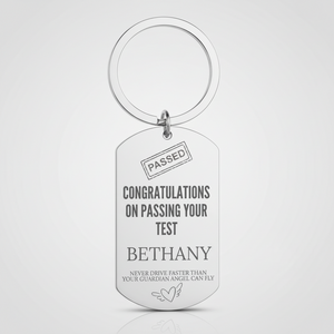 A silver metal dog tag keychain with a split key ring, featuring engraved personalized text that reads 'CONGRATULATIONS ON PASSING YOUR TEST BETHANY' and 'NEVER DRIVE FASTER THAN YOUR GUARDIAN ANGEL CAN FLY' on a light gray background.