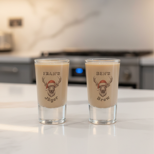 Two shot glasses with printed designs of deer wearing Santa hats on a kitchen counter.