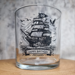 Personalised rum glass with ship design, custom name and age, shown with optional bamboo coaster and varnished wooden gift box – nautical themed gift for him