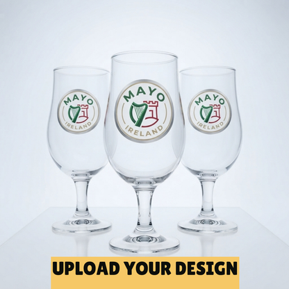 Three clear beer glasses with circular Mayo Ireland logos, shown on a light gray background with a yellow banner at the bottom reading 'UPLOAD YOUR DESIGN'.