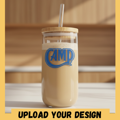 Glass tumbler with a wooden lid and straw, containing a creamy beverage with 'CAMP' logo, on a wooden surface.