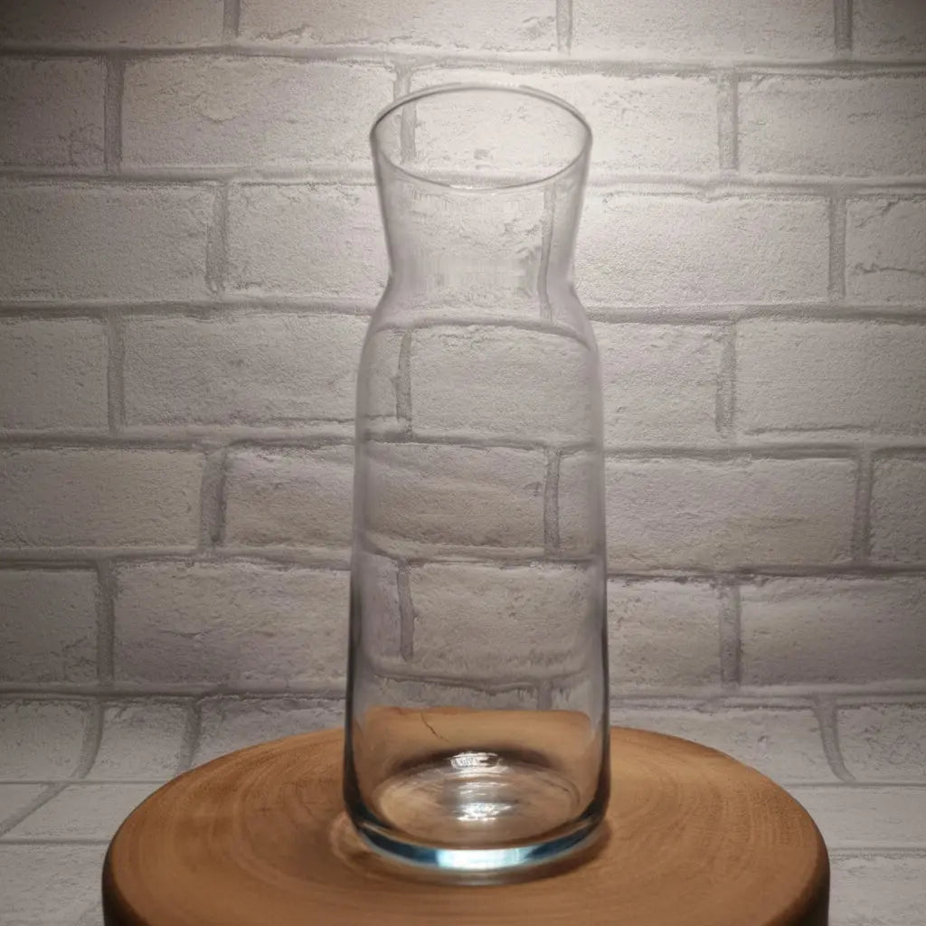 A Close up of custom printed text design on personalised glass carafe, upload your own design gifte with no contents, displayed on a wooden surface against a white brick wall background.