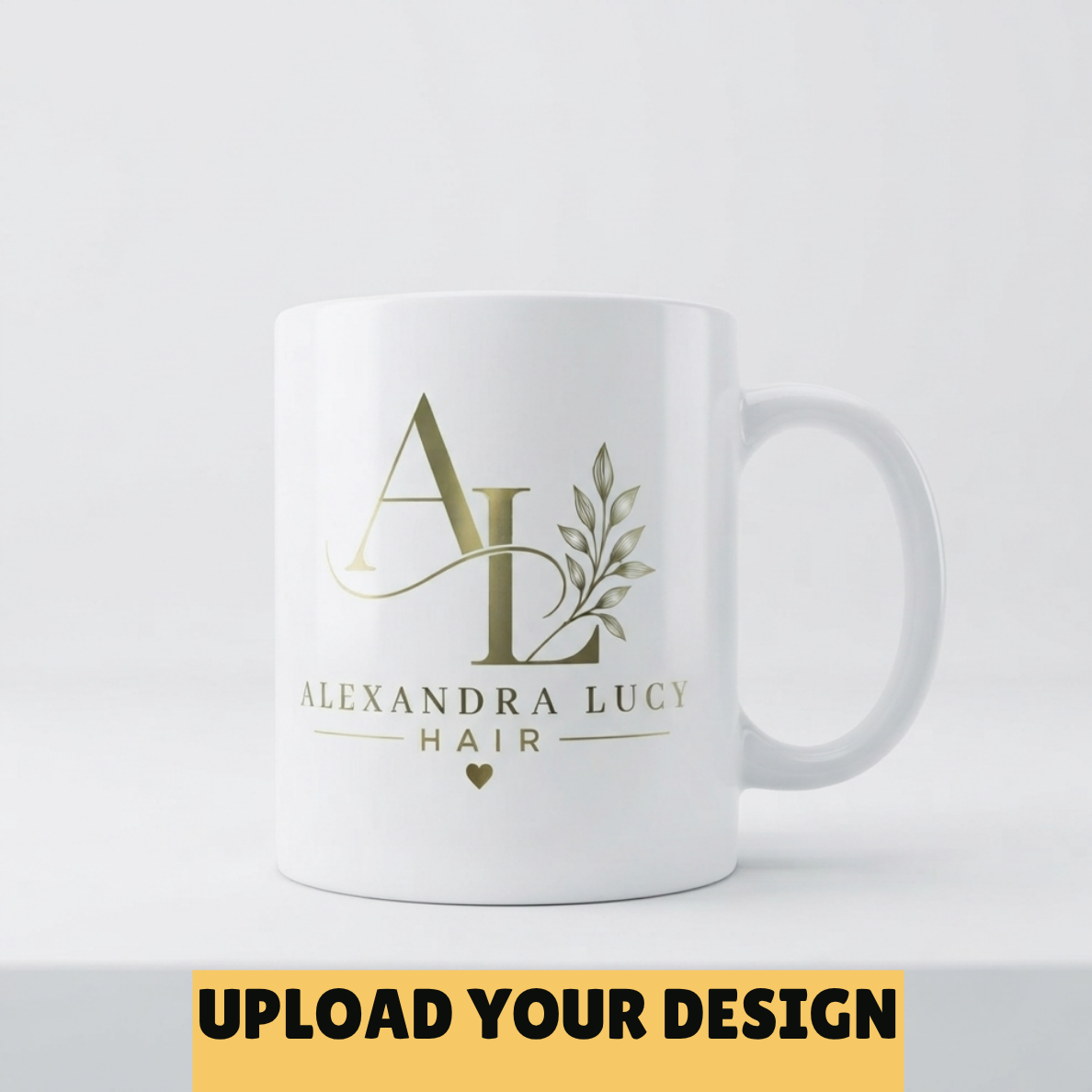 A white ceramic mug with a gold monogram logo and the text 'ALEXANDRA LUCY HAIR' on the front, shown on a light gray background. A yellow banner at the bottom reads 'UPLOAD YOUR DESIGN'.