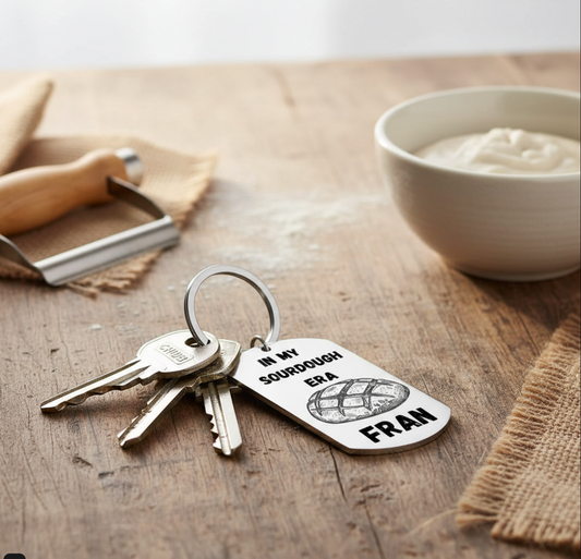 Keychain with 'In my sourdough era Fran' tag on a wooden surface with a bowl and rolling pin.