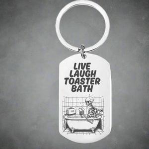 Dark humor stainless steel keyring with laser engraved “Live Laugh Toaster Bath” text and skeleton in bathtub design – edgy goth and emo gift accessory