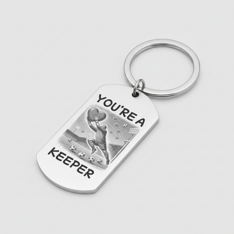 A silver metal dog tag keychain with a key ring, featuring a black and white illustration of a soccer player and the text 'YOU'RE A KEEPER' on a light gray background.